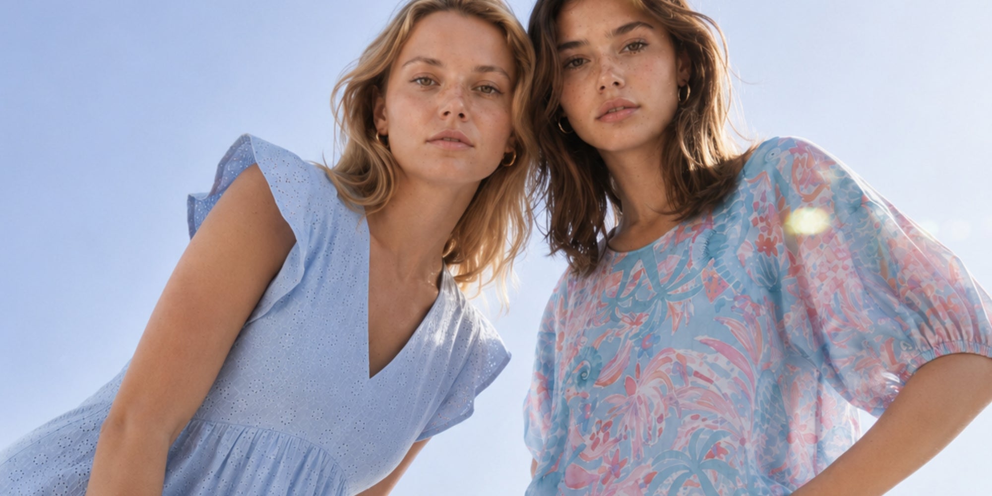 Zwei Frauen tragen sommerliche Outfits in hellen Blau- und Pastellfarben vor strahlendem Himmel. Die luftigen Materialien und femininen Designs verleihen dem Look eine leichte, elegante und moderne Ausstrahlung.
