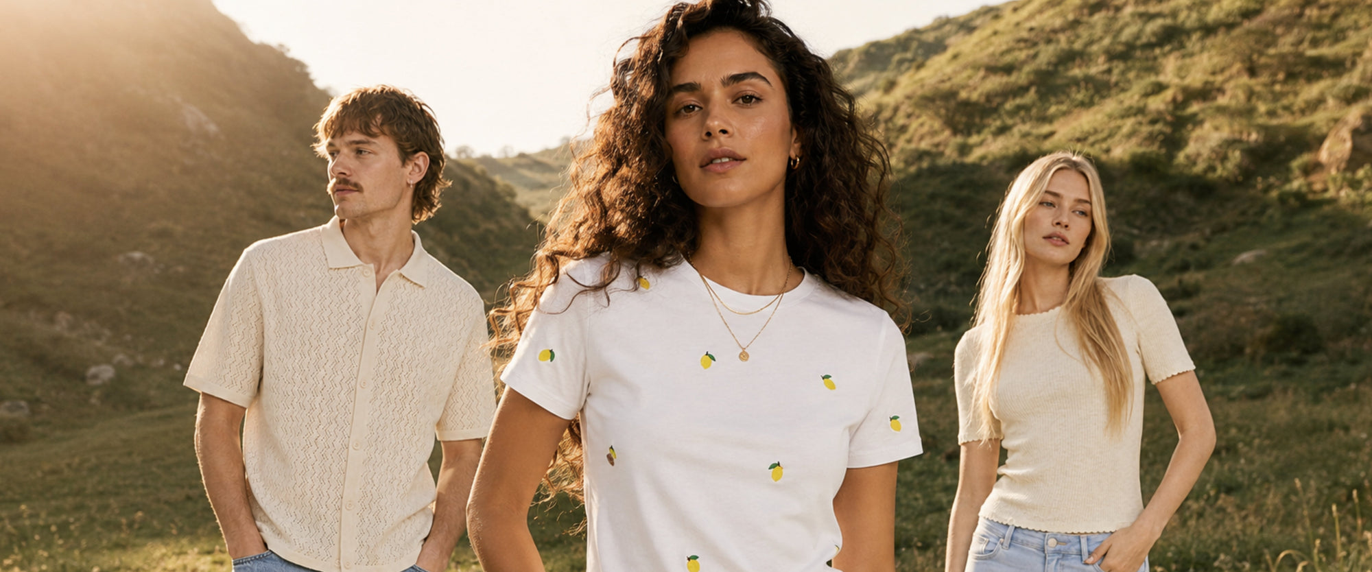 Drei Models in nachhaltigen Casual-Looks auf einer sonnigen grünen Wiese – natürliche Farben, moderne Mode und entspannter Lifestyle in einer idyllischen Landschaft.